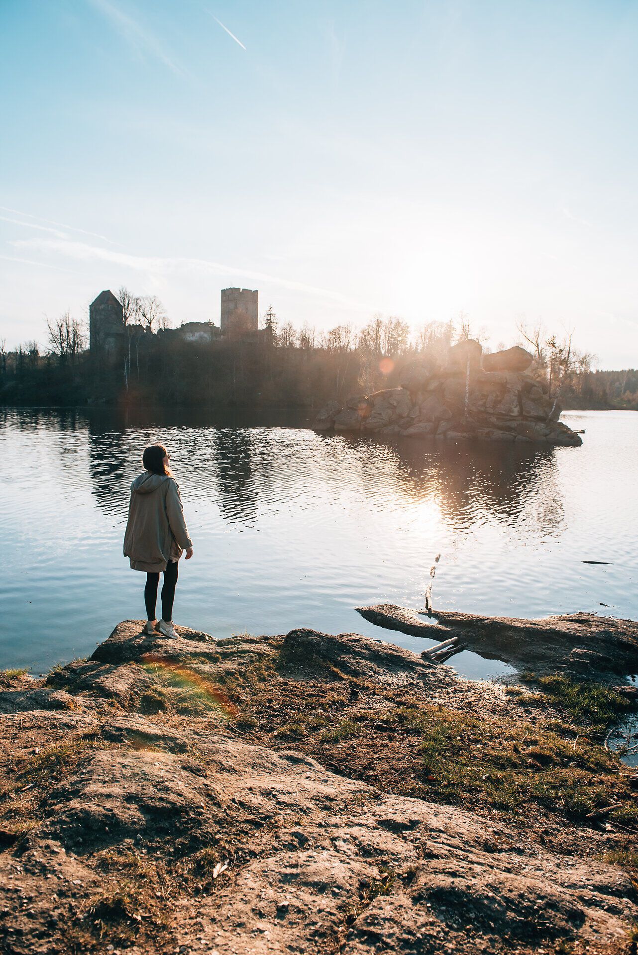 Am Ufer eines glitzernden Sees steht eine Person und genießt den atemberaubenden Blick auf die sanften Hügel im Hintergrund. Die warmen Sonnenstrahlen tauchen die Landschaft in ein goldenes Licht und schaffen eine friedliche Atmosphäre, die zum Verweilen einlädt.