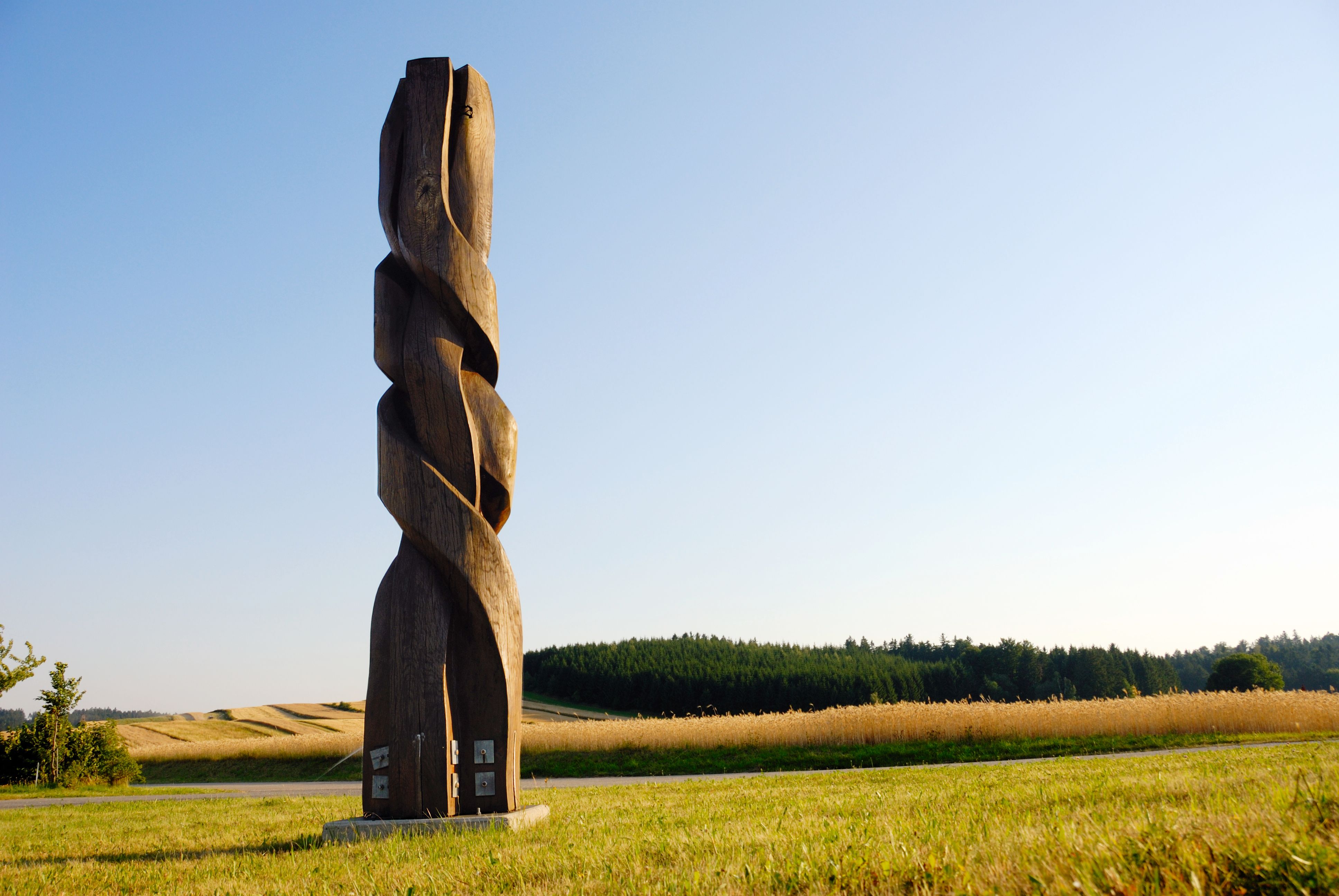 Holzskulptur auf einem Feld mit blauem Himmel im Hintergrund.
