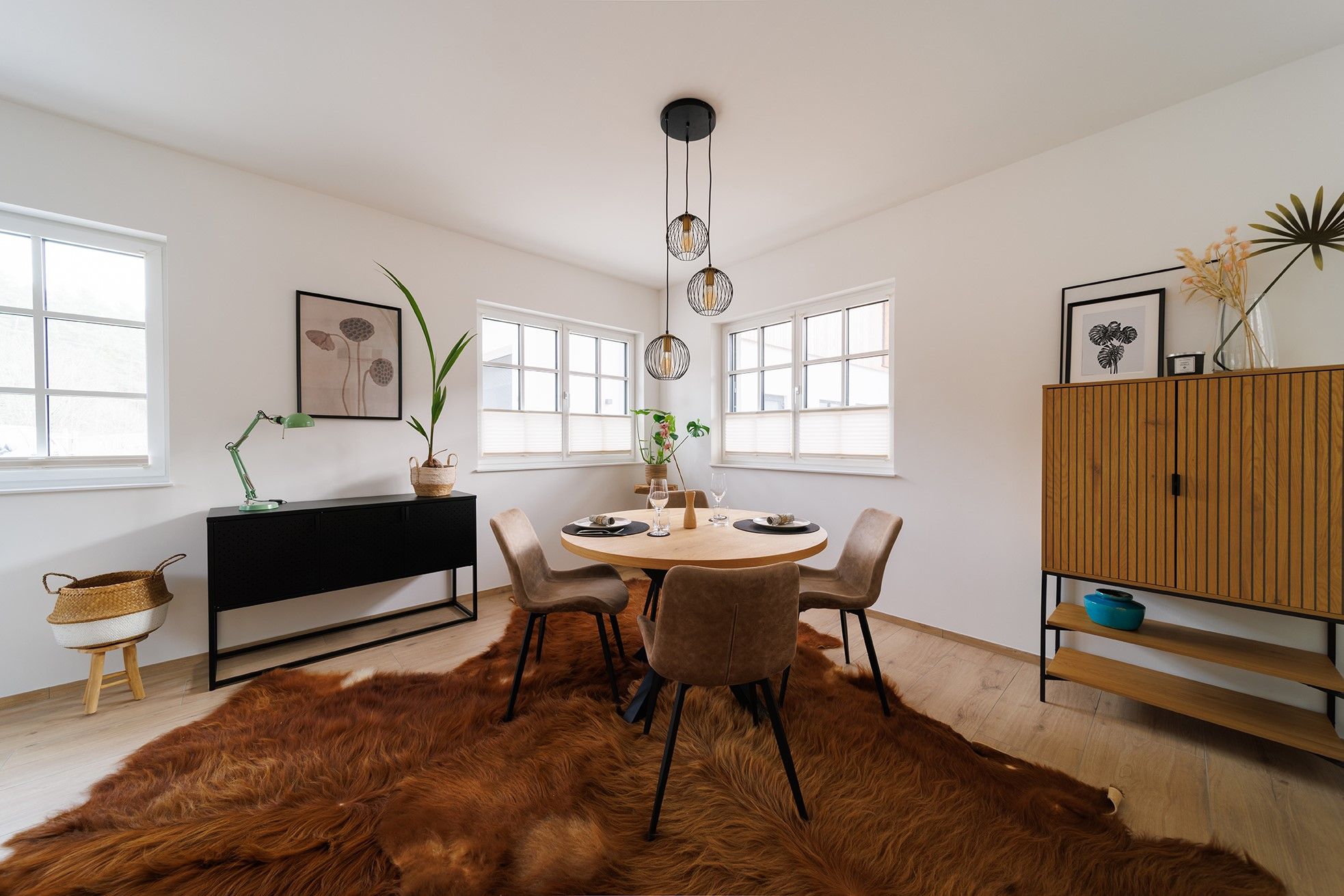 Modernes Esszimmer mit rundem Tisch, vier Stühlen, Fellteppich und minimalistischer Dekoration.