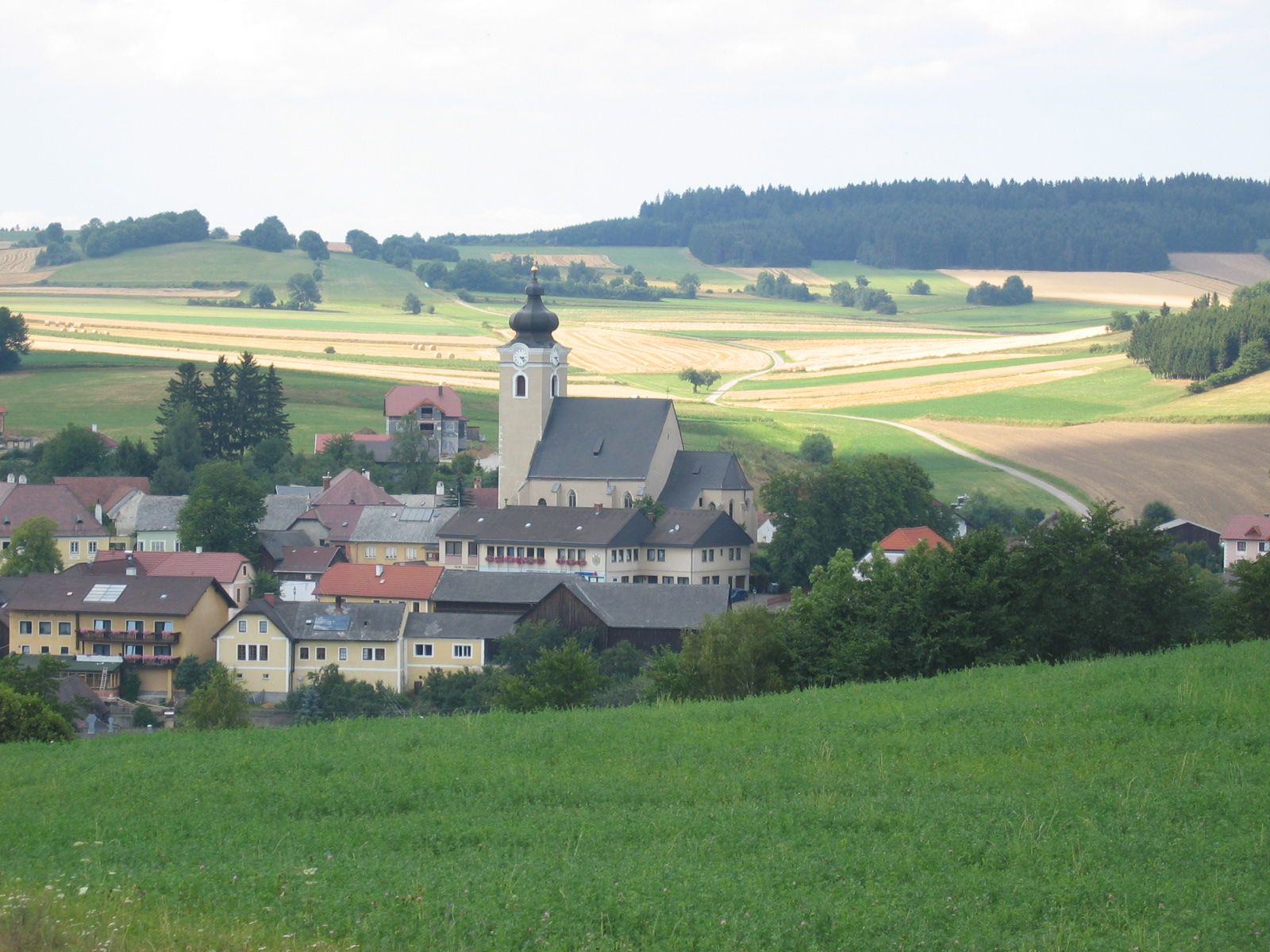 Ländliche Gemeinde mit Kirche und Feldern im Hintergrund.
