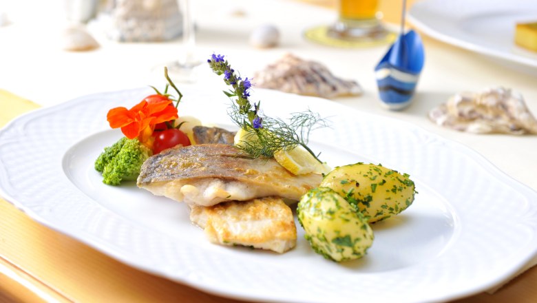 A plate of fried fish fillet, potatoes and vegetables, decorated with herbs and flowers.