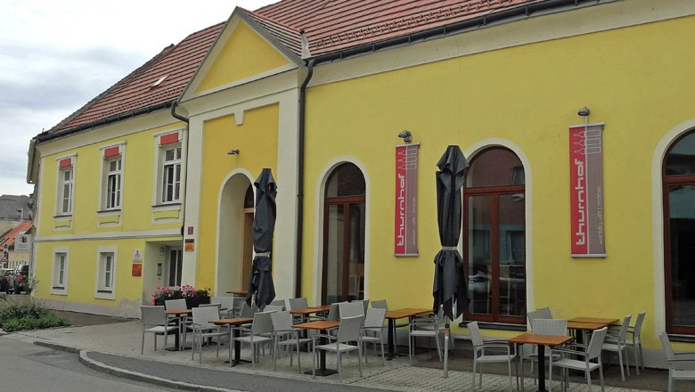 Gelbes Geb&auml;ude mit Terrasse und Tischen vor der Weinbar Thurnhof in Horn.