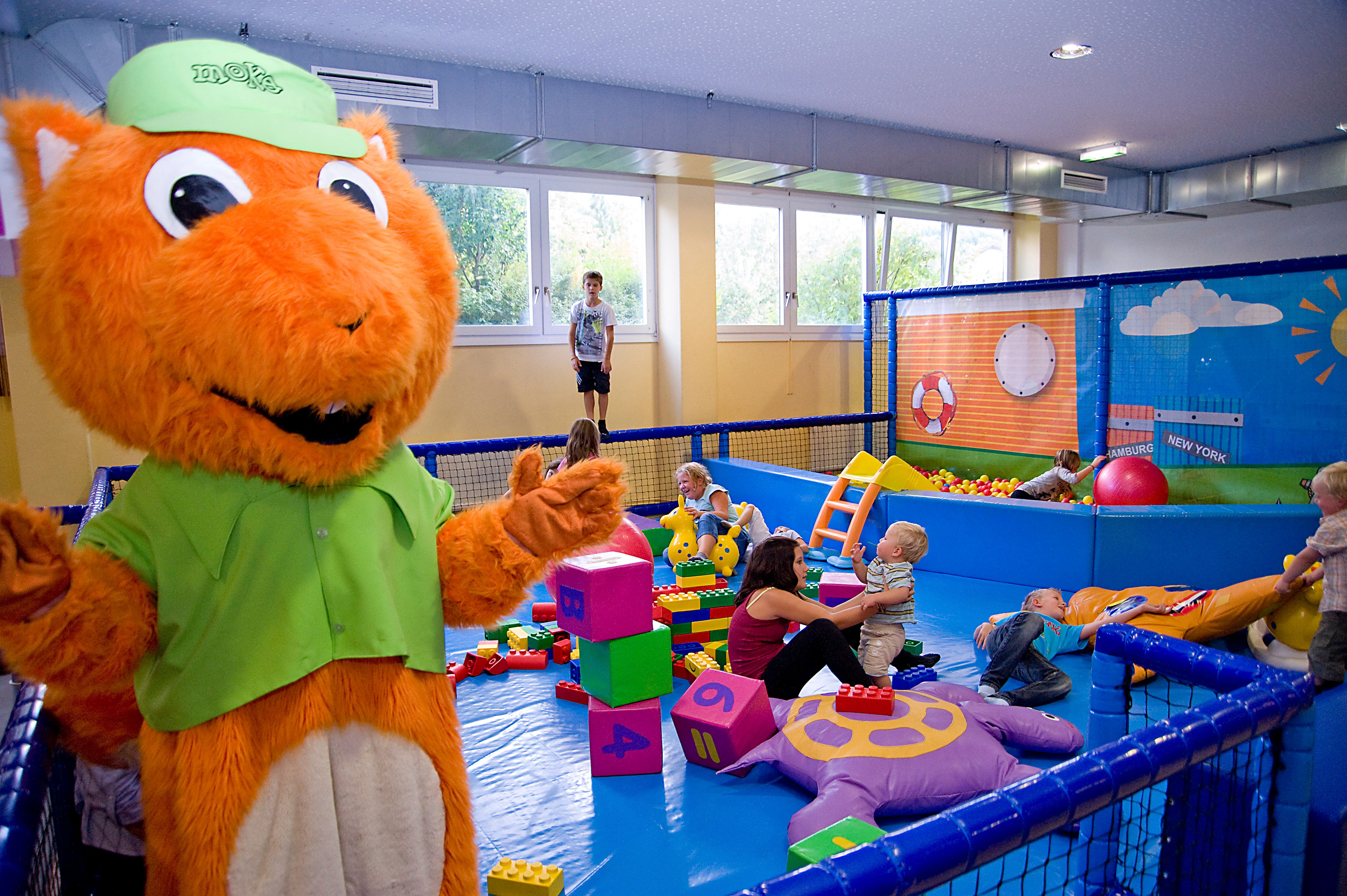 Kinder spielen in einem Indoor-Spielbereich mit einem großen orangefarbenen Maskottchen.