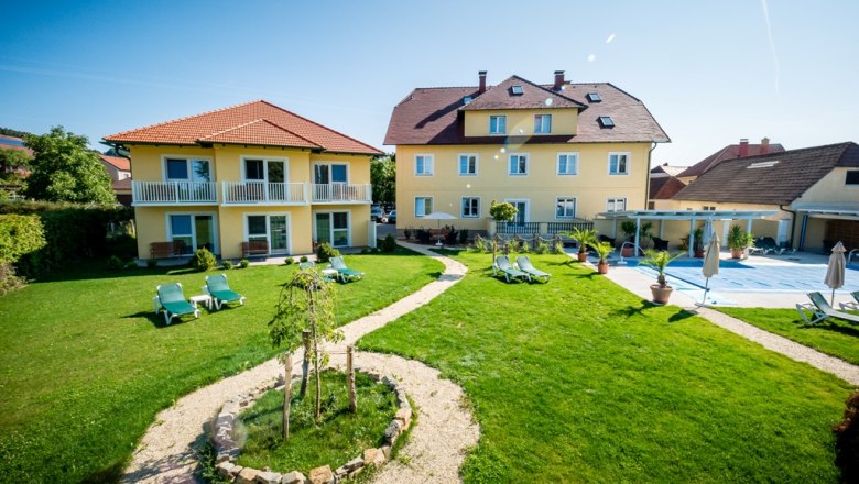 Gartenanlage Dorfhotel Grüner Baum, © Photography Pfeffel Gartenanlage mit gelben Gebäuden und Liegestühlen bei sonnigem Wetter.