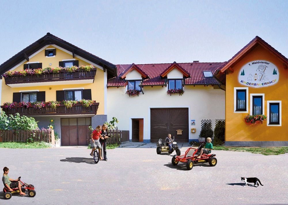 Kinder spielen auf Kettcars vor einem gelben Bauernhof mit Blumenbalkonen.