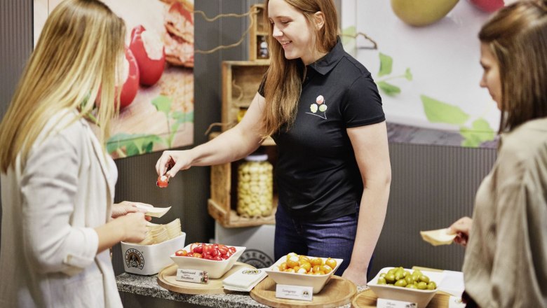 A woman offers two other women various stuffed peppers and olives to taste.