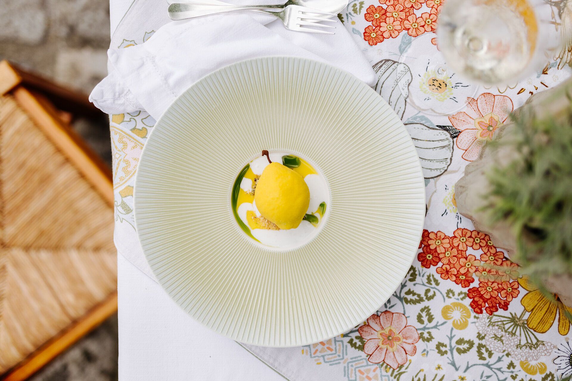 Ein kunstvoll angerichteter Teller mit einer erfrischenden Zitronensorbet-Kreation lädt zum Genießen ein. Umgeben von einer blühenden Tischdecke und dem sanften Licht des Tages, vermittelt die Szenerie ein Gefühl von Sommerfrische und kulinarischem Genuss.