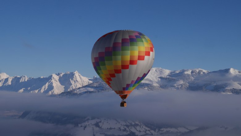 Heißluftballon über schneebedeckten Bergen und Wolken.