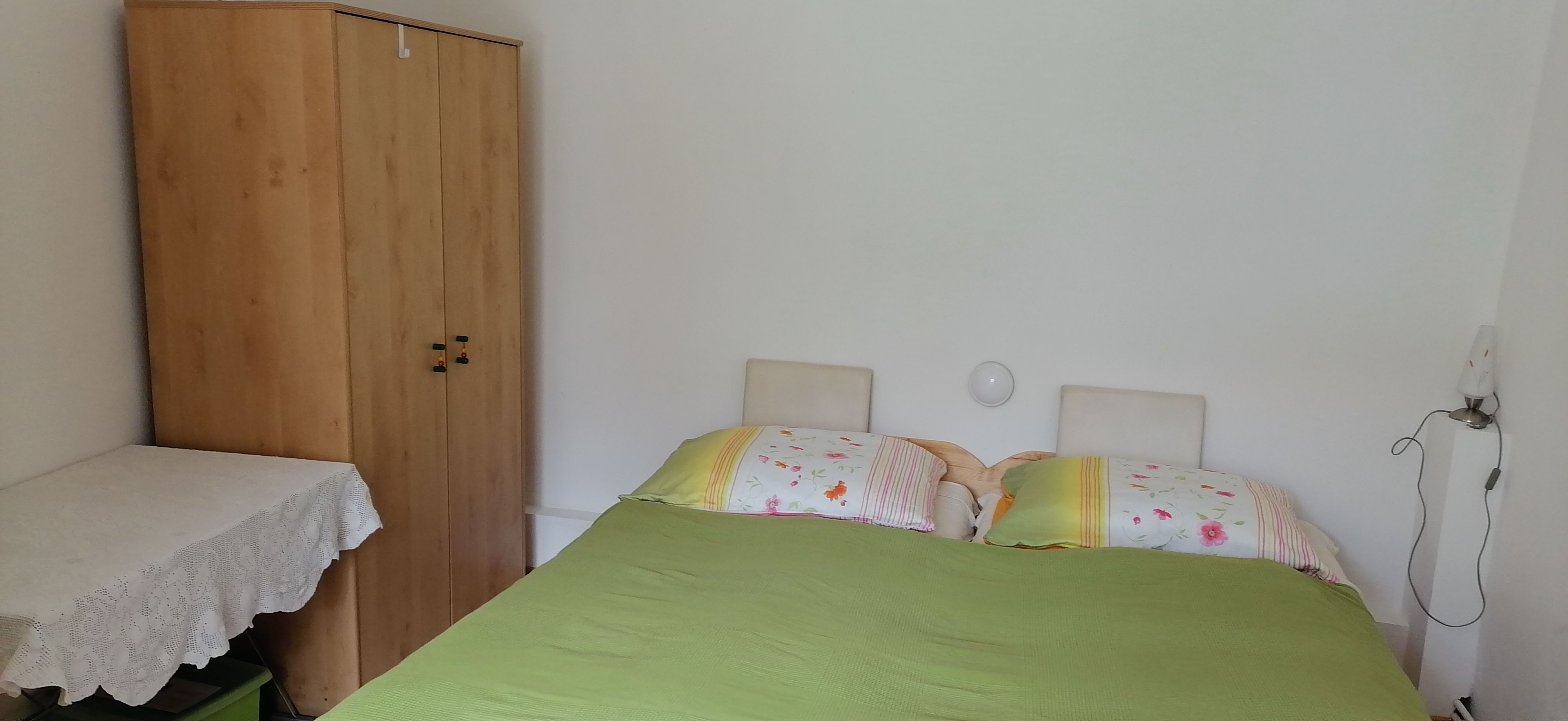 Ein Schlafzimmer mit einem Doppelbett, einem Holzschrank und einem Tisch mit weißer Tischdecke.
