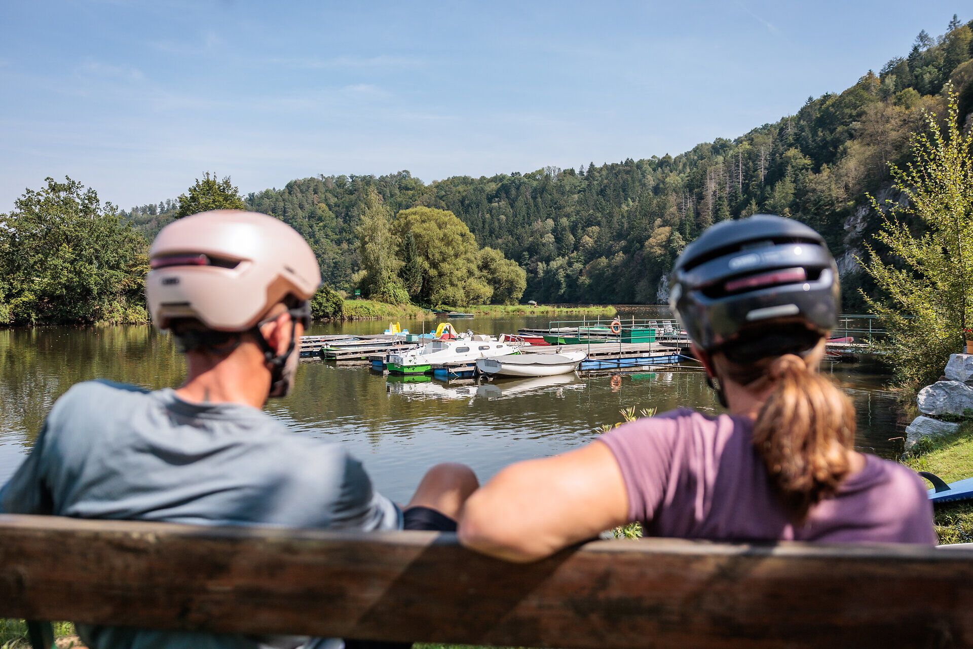 Die sanfte Brise streicht über den glitzernden Stausee, während Radfahrer auf einer Bank entspannen und die malerische Landschaft genießen. Umgeben von üppigem Grün und sanften Hügeln, lädt dieser Ort dazu ein, die Seele baumeln zu lassen und die Schönheit der Natur zu erleben.