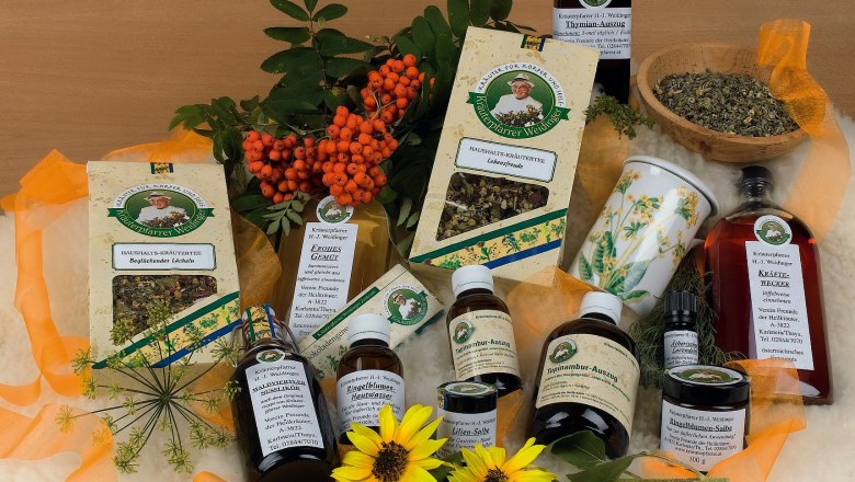 Verschiedene Kräuterprodukte von Kräuterpfarrer Weidinger, umgeben von Blumen und Beeren.