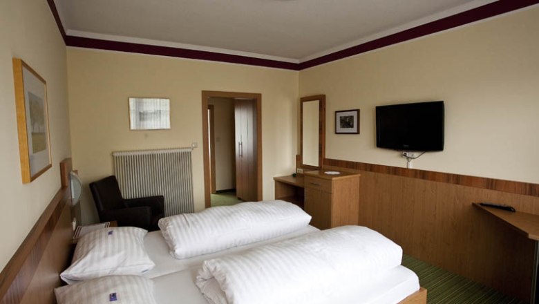 Hotelzimmer mit Doppelbett, TV, Schreibtisch und Spiegel.