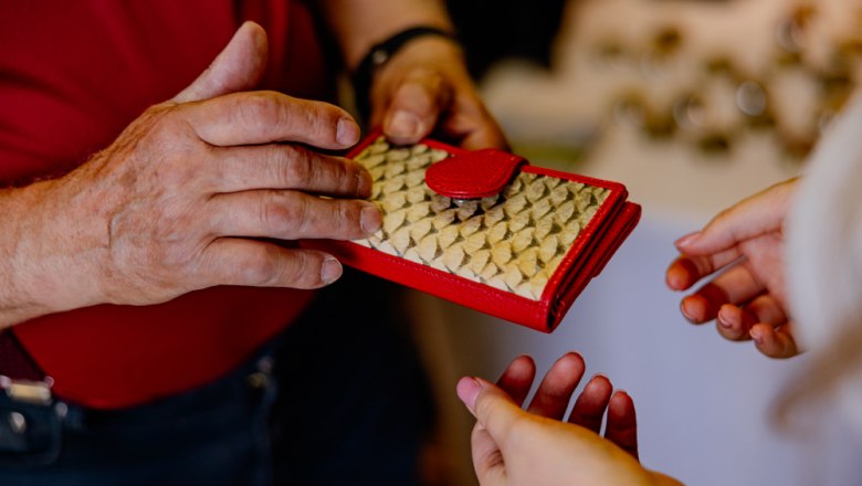 Zwei Personen halten eine Geldbörse aus Fischleder mit roten Akzenten.