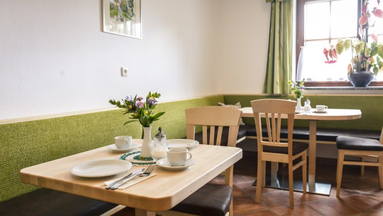 Gemütlicher Frühstücksraum mit Holztischen, grünen Bänken und Blumen auf dem Tisch.