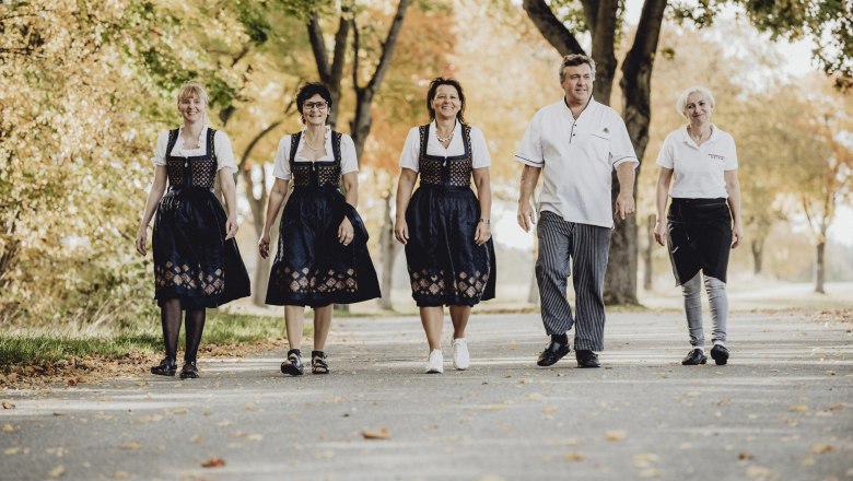 Fünf Personen in traditioneller Kleidung gehen auf einer von Bäumen gesäumten Straße.