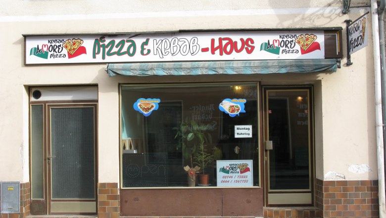 Fassade eines Pizza- und Kebab-Restaurants mit Schildern und Fenstern.
