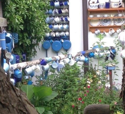 Ein Garten mit vielen bunten Tassen, die an Wänden und Stangen hängen.