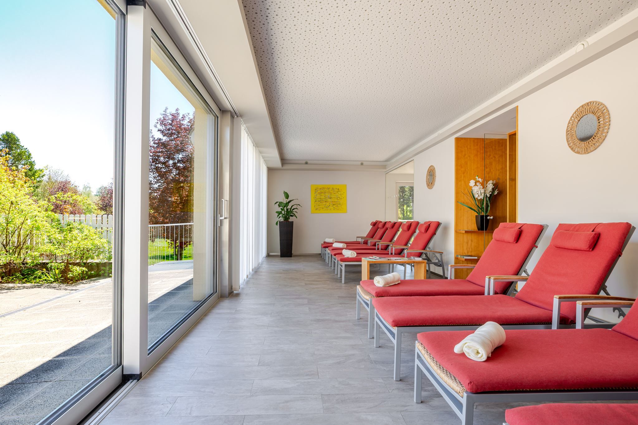 Ruheraum im Hotel Ottenstein mit roten Liegen, großen Fensterfronten und Blick ins Grüne.