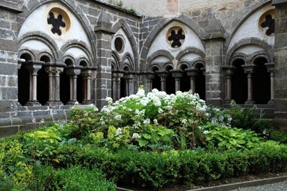 Ein mittelalterlicher Kreuzgang mit Rundbögen und einem zentralen Garten mit Blumen und Sträuchern.