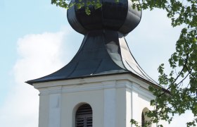 Kirchturm mit Zwiebelhaube und grünen Blättern im Vordergrund.
