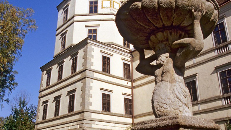 Ein historisches Gebäude mit Turm und eine steinerne Statue im Vordergrund.
