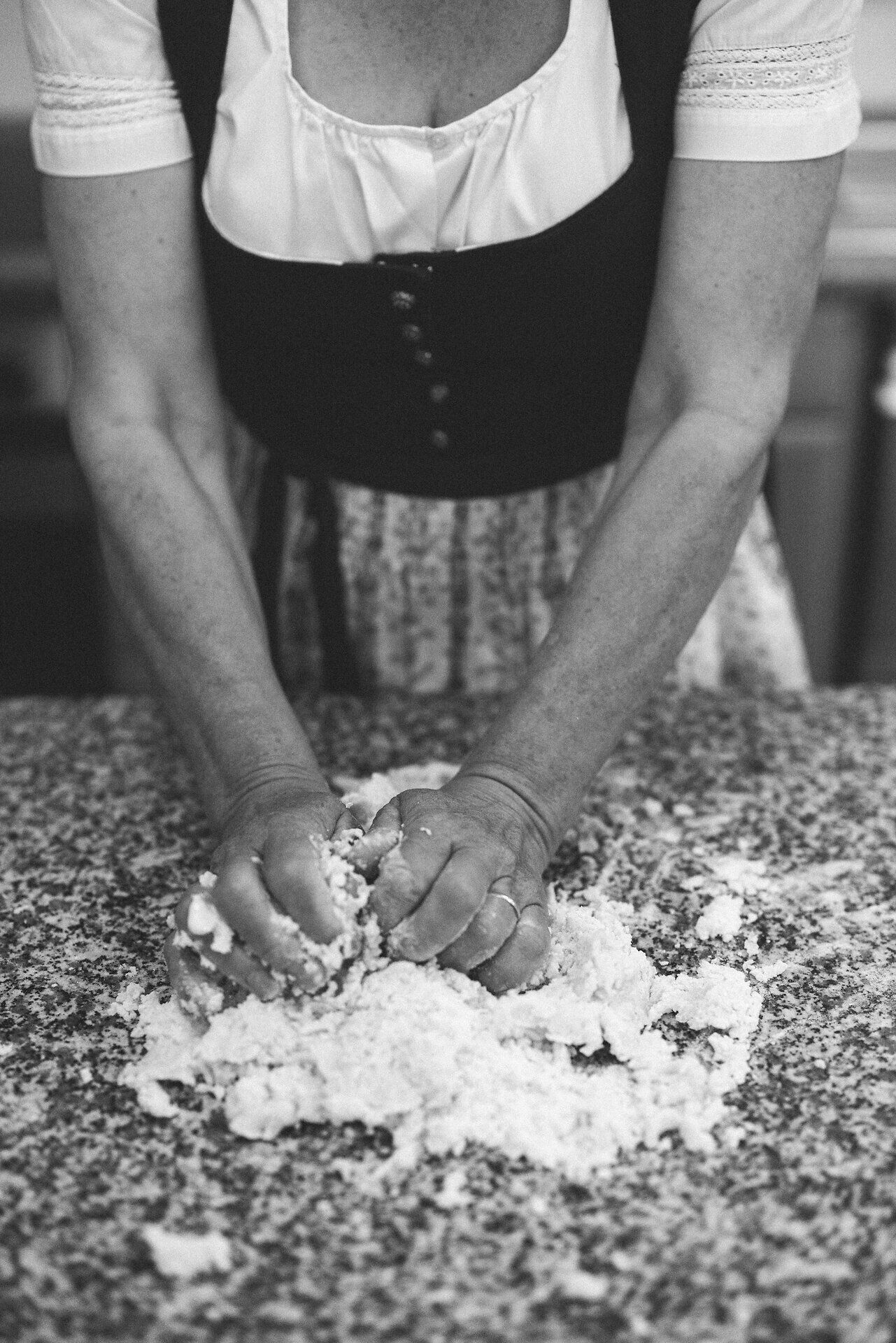 In einer einladenden Küche werden mit Hingabe Mohnnudeln aus frischem Kartoffelteig zubereitet. Die Hände kneten den Teig, während der Duft von frisch gebackenem Brot die Luft erfüllt und eine warme, familiäre Atmosphäre schafft.