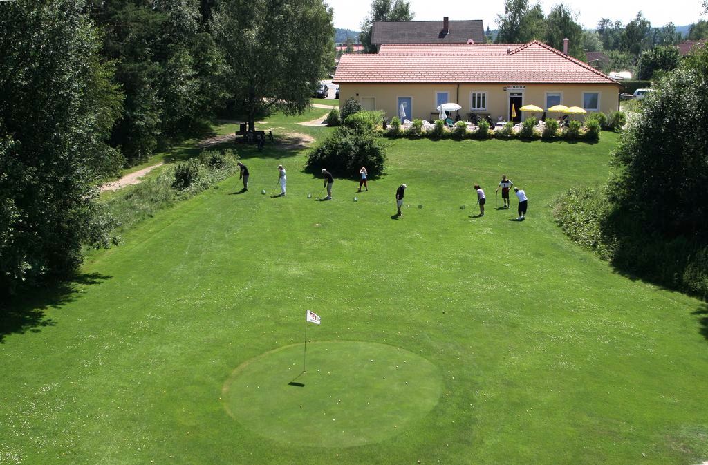 Golfplatz mit Spielern und Clubhaus im Hintergrund.