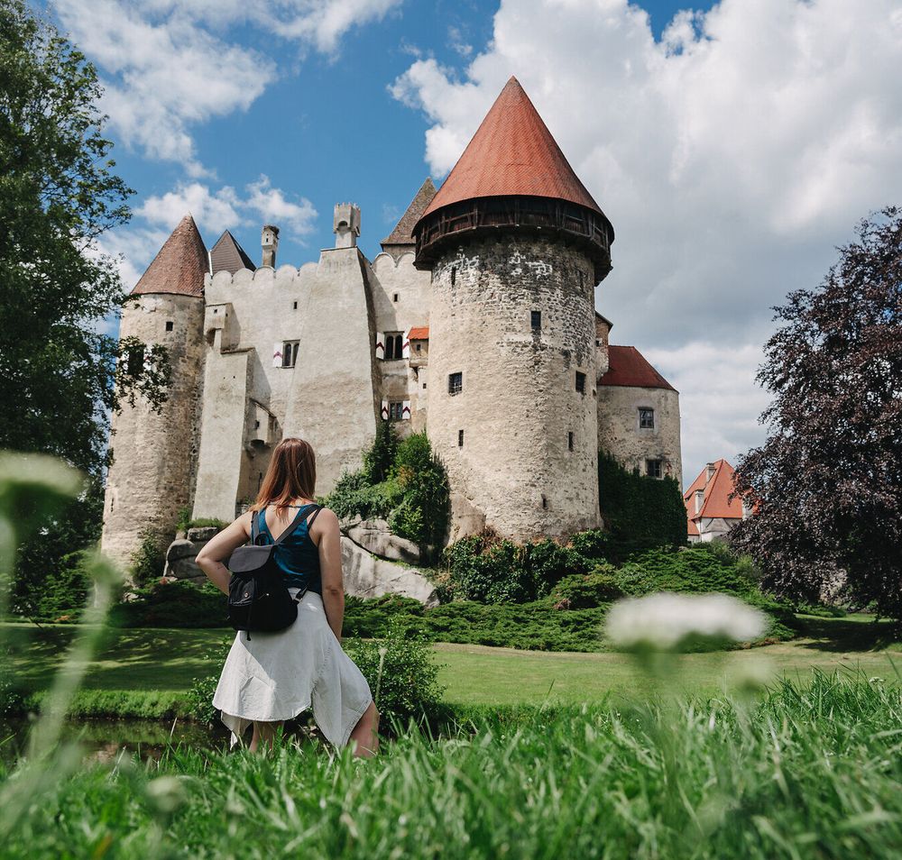 Die majestätische Burg Heidenreichstein thront eindrucksvoll über der sanften Landschaft, umgeben von üppigem Grün und blühenden Wiesen. Ein sanfter Wind weht durch die Bäume, während die Wolken am strahlend blauen Himmel vorbeiziehen und eine friedliche Atmosphäre schaffen, die zum Verweilen einlädt.