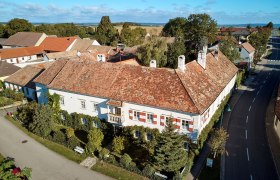 Luftaufnahme eines historischen Geb&auml;udes mit roten Ziegeld&auml;chern und wei&szlig;en Fassaden, umgeben von B&auml;umen und Stra&szlig;en.