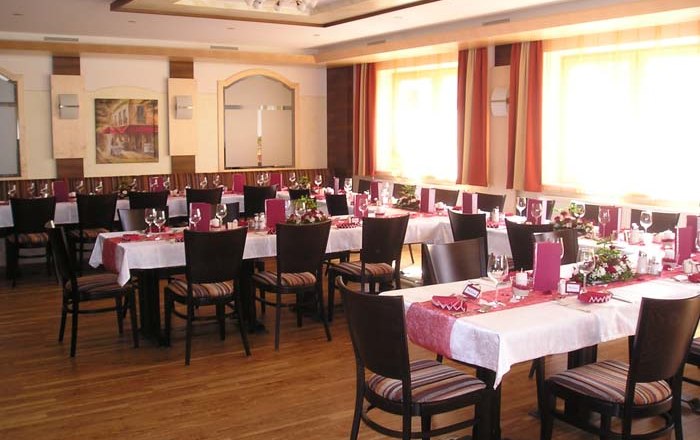 Ein elegant gedeckter Speisesaal mit mehreren Tischen, roten Tischläufern und Stühlen.