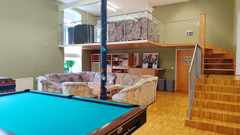 Ein Jugendraum mit Billardtisch, Sofas und einer Empore mit Treppe.