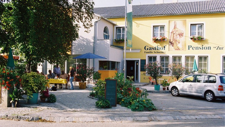 Gasthof-Pension "Zur Hammerschmiede", © Ludwig Schneider A yellow building with the inscription 'Gasthof-Pension Zur Hammerschmiede'. There are tables, chairs and a car in front of the building.