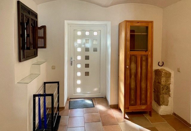 Eingangsbereich mit weißer Tür, Holzschrank und Fliesenboden.