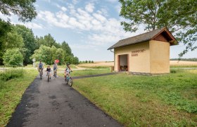 Eine Familie fährt mit Fahrrädern auf einem Weg neben einem gelben Gebäude mit der Aufschrift 'Oberndorf-Raabs'.