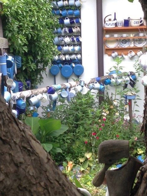 Ein Garten mit vielen bunten Tassen, die an Wänden und Stangen hängen.