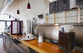 Innenansicht eines Cafés mit Theke, Kaffeemaschine und Gläsern.