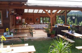 Ein gemütlicher Biergarten mit Holztischen und Bänken, dekoriert mit Sonnenblumen, umgeben von grüner Landschaft.