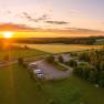 Luftaufnahme eines Wohnmobilstellplatzes bei Sonnenuntergang, umgeben von Feldern und Wäldern.