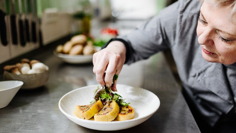 A woman arranges food and salad on a plate.
