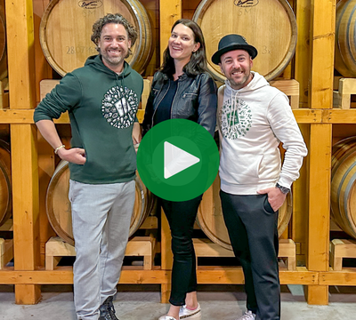 3 Personen vor Whiskyfässern lachend in die Kamera