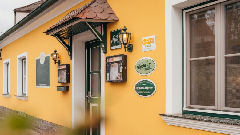 Yellow building with door and windows, signs and lanterns on the wall.