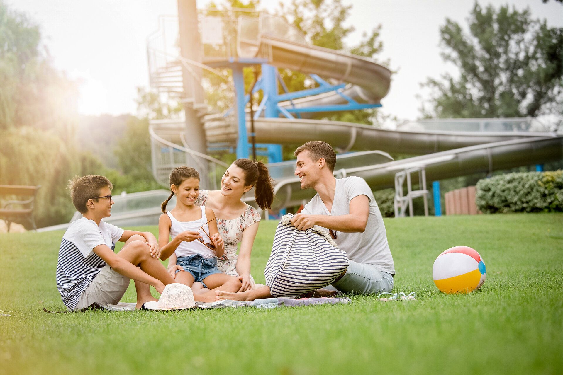 Eine fröhliche Familie genießt einen entspannten Tag im Freien, umgeben von saftigem Grün und der warmen Sonne. Die Kinder spielen mit einem bunten Ball, während die Erwachsenen sich unterhalten und die Natur genießen. Diese harmonische Atmosphäre lädt dazu ein, die Schönheit der Umgebung zu erkunden.