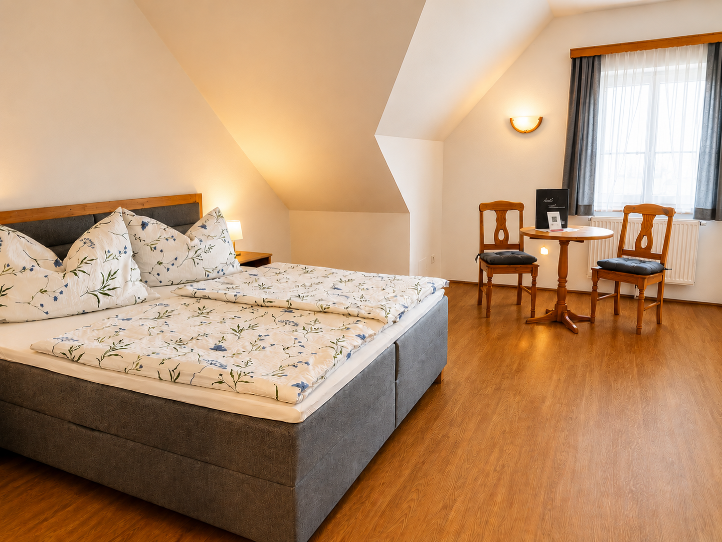 Gemütliches Schlafzimmer mit Doppelbett, Holzboden und kleinem Tisch mit zwei Stühlen.
