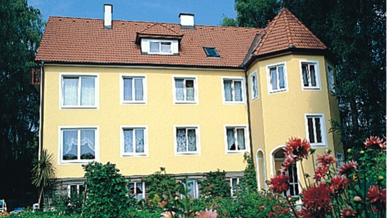 Gelbes Haus mit rotem Dach und Garten im Vordergrund.