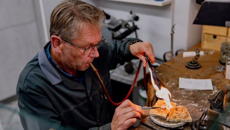 Ein Mann arbeitet mit einem Brenner an einem Schmuckst&uuml;ck in einer Werkstatt.