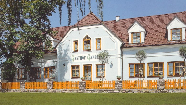 Ein traditionelles Gasthaus mit weißer Fassade und roten Dachziegeln, umgeben von Bäumen und einem Holzzaun.