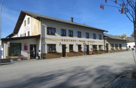 Gasthof Mader an einer ruhigen Straße mit blühenden Blumenkästen und blauem Himmel.