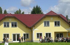 Gelbes Gebäude mit rotem Dach, Menschen sitzen draußen an Tischen.