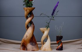 Drei gedrehte Holzvasen mit Blumen vor grauem Hintergrund.