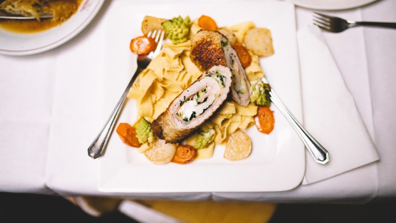 Gefülltes Fleisch auf Nudeln mit Gemüse auf einem weißen Teller.